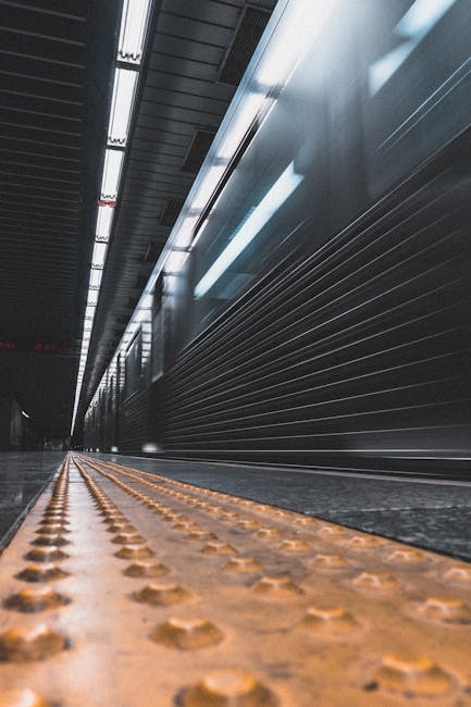 The image shows an indoor stairwell area within a public transport station, with a downward view of the staircase leading to an underground passage. The staircase has metallic railings and steps, and 